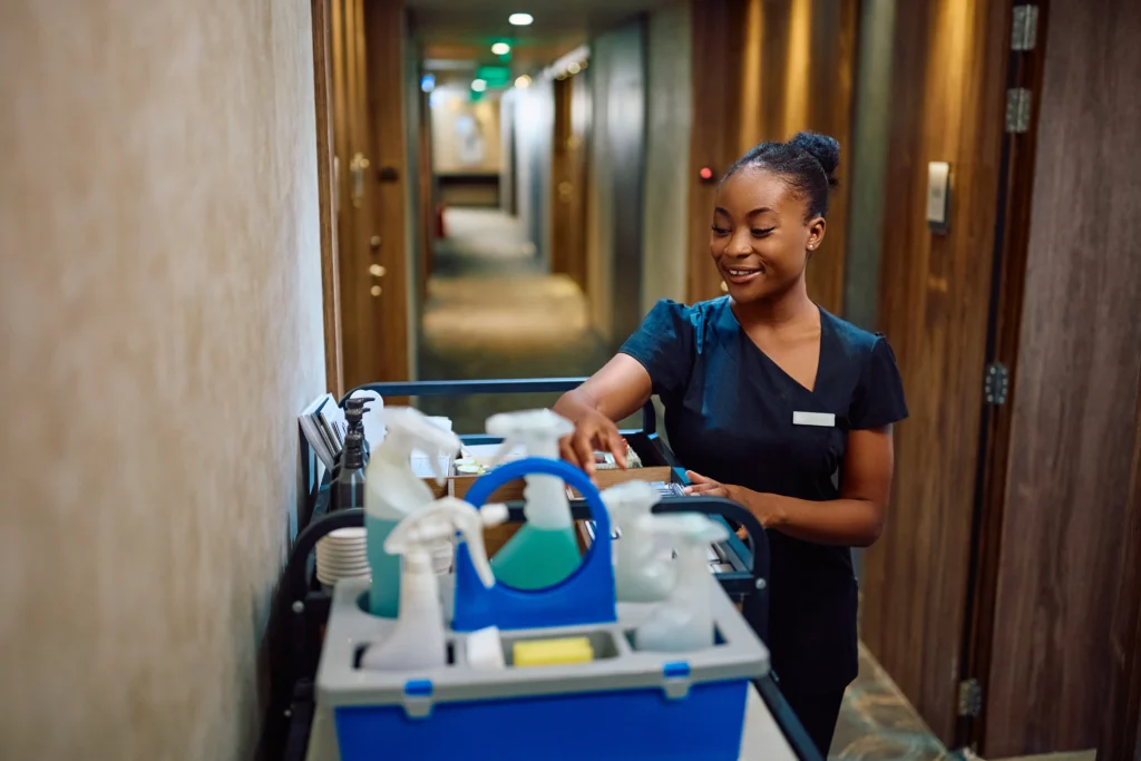 Camarera avanzando por los pasillos con carrito abastecido de productos de limpieza para hoteles.