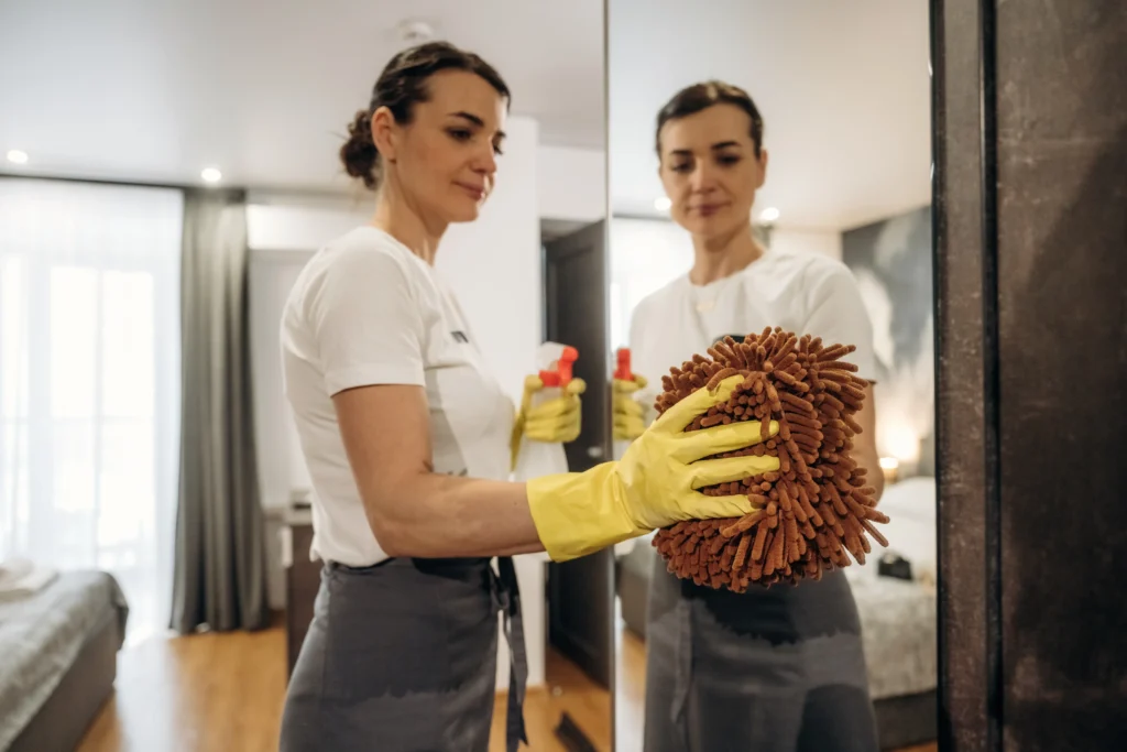 Mujer realizando limpieza en hoteles, limpiando un cristal con paño y un producto especializado para mayor higiene.